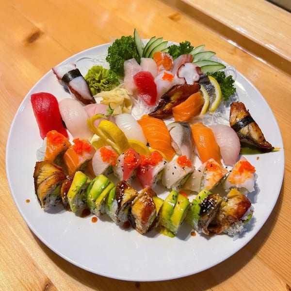 A large white platter filled with various colorful sushi, sashimi, and rolls on a wooden table.