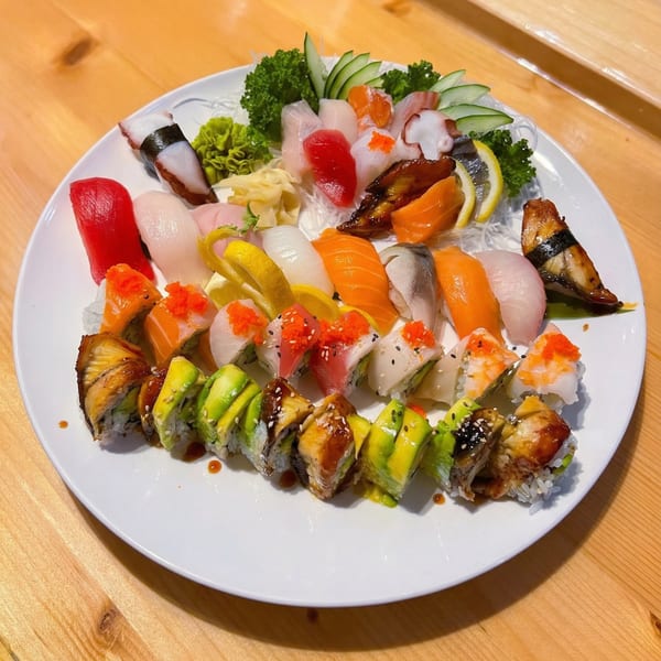 A large white platter filled with various colorful sushi and sashimi, including rolls topped with avocado.