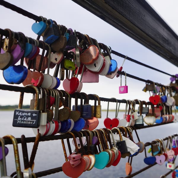 Numerous colorful heart-shaped and traditional padlocks are attached to a metal railing over water.