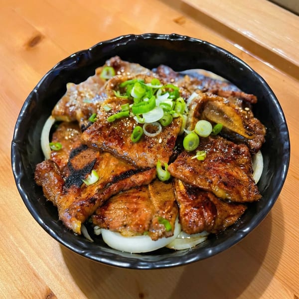 A black bowl of Izziban's Korean BBQ short ribs with onions and green onions on a wooden table.